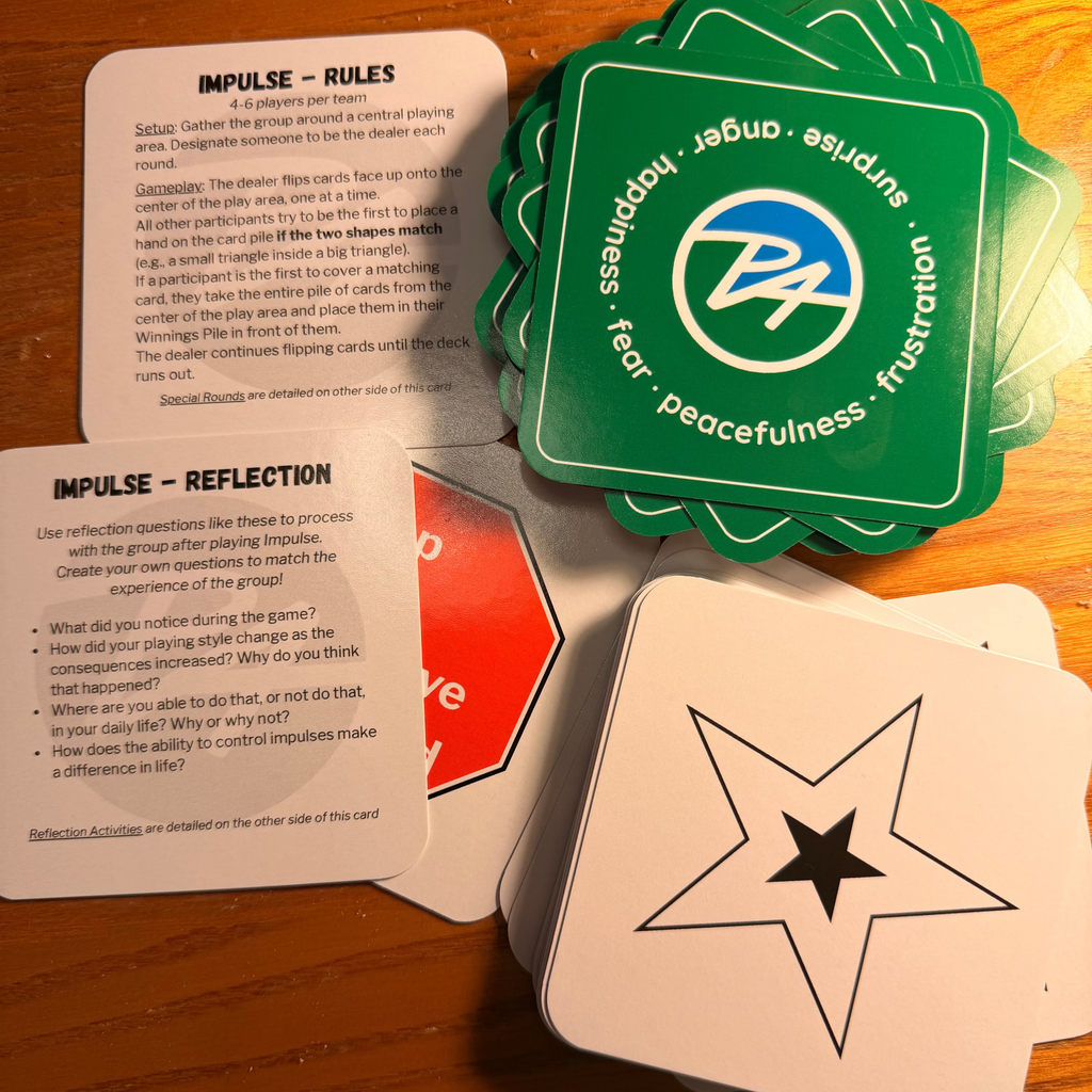 A set of square cards laid out on a wooden tabletop, including white cards with black text and symbols, a green card stack with a blue and white logo, and a red-and-white card partially visible underneath.