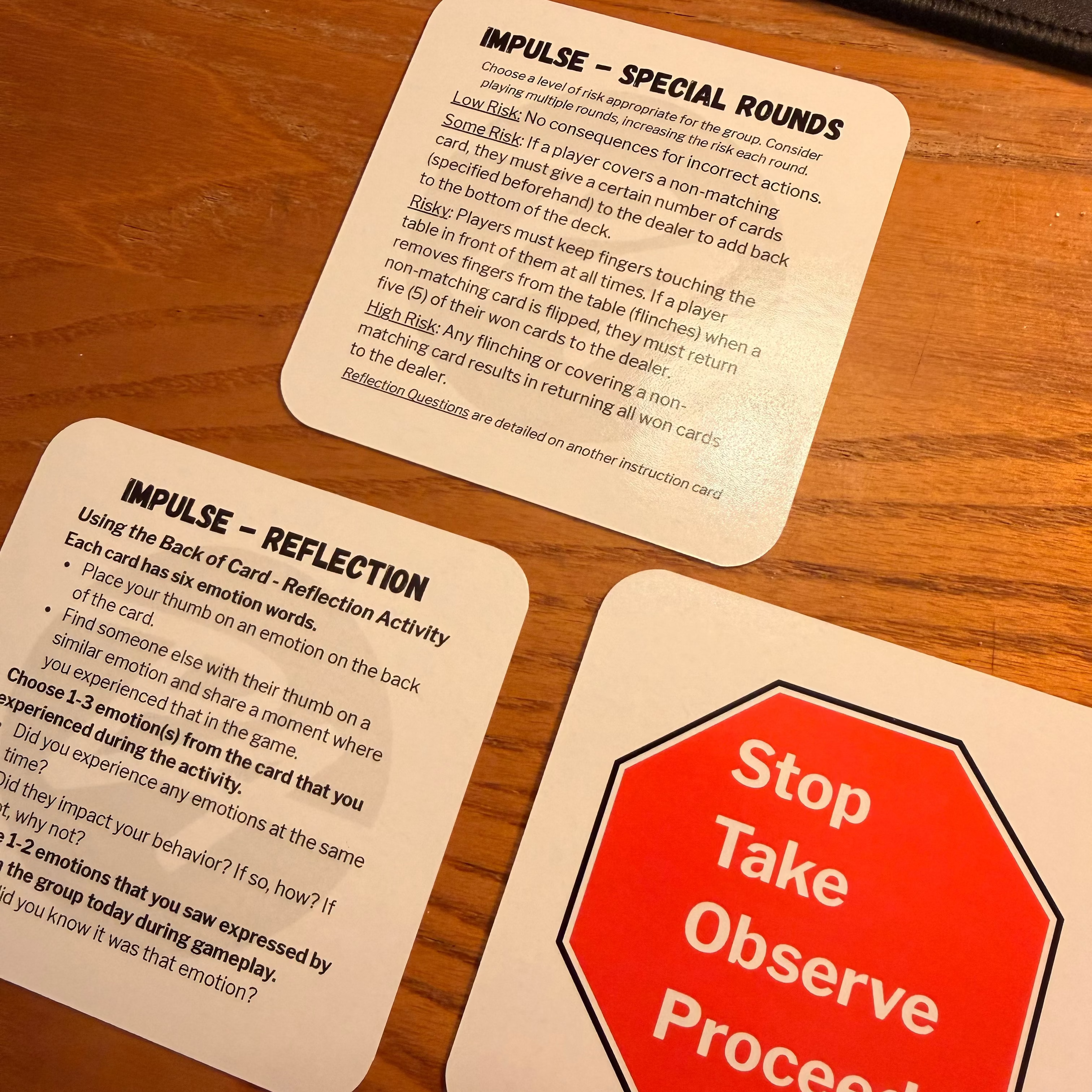 Three printed cards laid on a wooden tabletop. One card shows a red octagonal stop sign style graphic with white text reading 'Stop Take Observe Proceed.